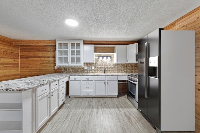 kitchen featuring stainless steel gas stove, refrigerator with ice dispenser, open shelves, white cabinetry, and a peninsula