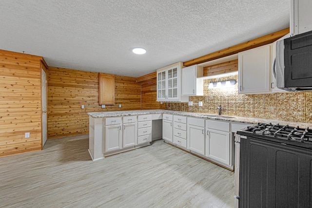 kitchen with stainless steel microwave, a peninsula, light wood-style floors, white cabinetry, and a sink