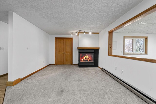 unfurnished living room with baseboard heating, track lighting, baseboards, and a glass covered fireplace