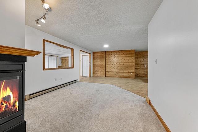 unfurnished living room featuring a baseboard radiator, track lighting, a textured ceiling, a glass covered fireplace, and carpet flooring