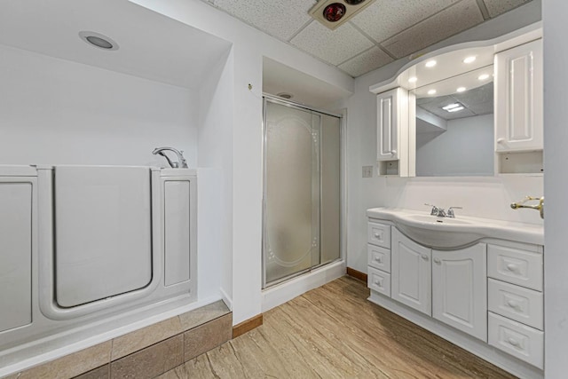 bathroom featuring vanity, a shower stall, wood finished floors, and a paneled ceiling