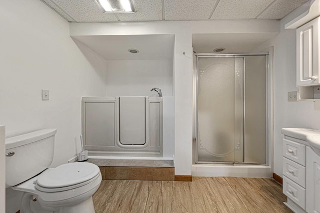 bathroom with a shower stall, toilet, wood finished floors, and a paneled ceiling