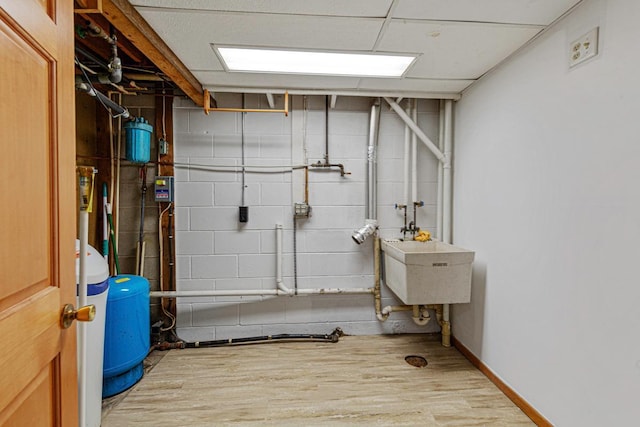 basement featuring a sink, wood finished floors, baseboards, concrete block wall, and a paneled ceiling