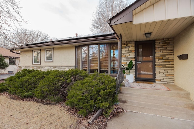 doorway to property featuring stucco siding, stone siding, board and batten siding, and solar panels