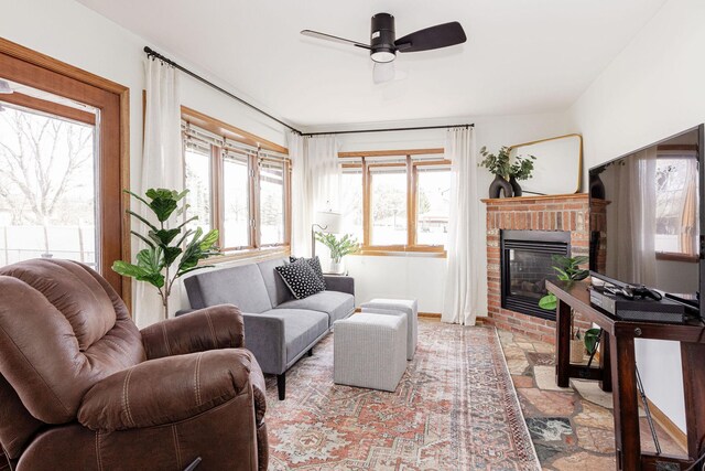 living room with a brick fireplace, baseboards, and ceiling fan