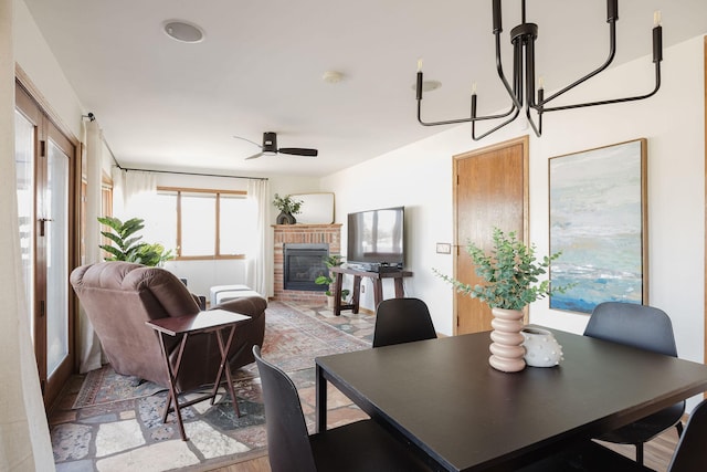 dining space with ceiling fan with notable chandelier and a fireplace