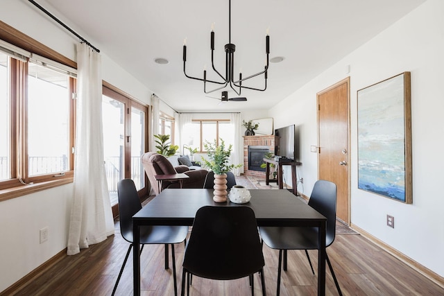 dining space with baseboards, a notable chandelier, a brick fireplace, and wood finished floors