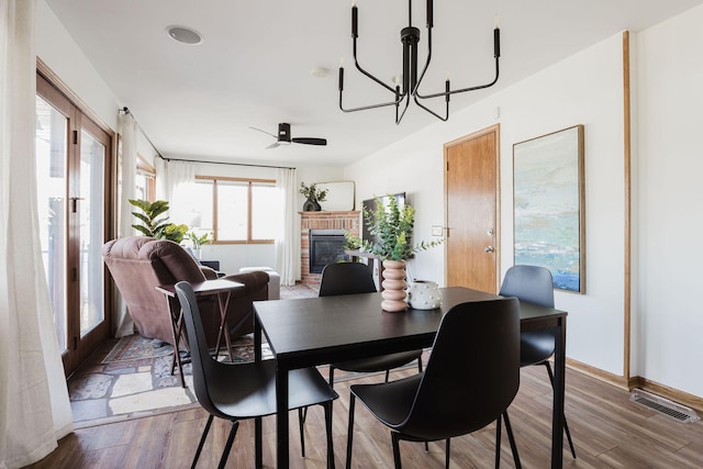 dining room with visible vents, ceiling fan with notable chandelier, wood finished floors, a fireplace, and baseboards