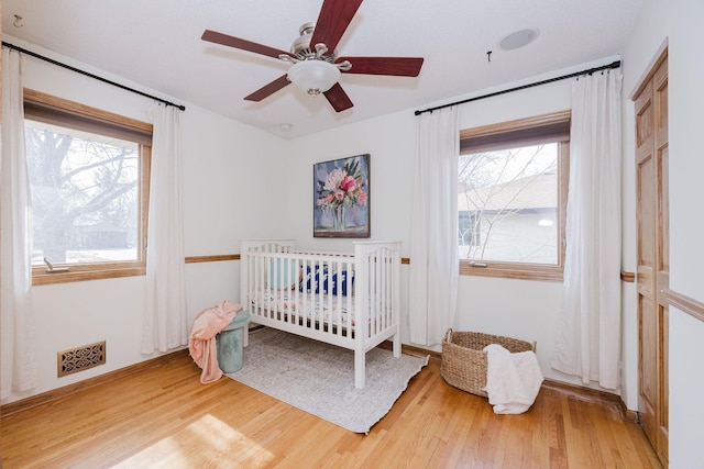 bedroom with a crib, multiple windows, wood finished floors, and visible vents