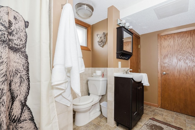 full bath with toilet, vanity, a textured ceiling, and tile walls