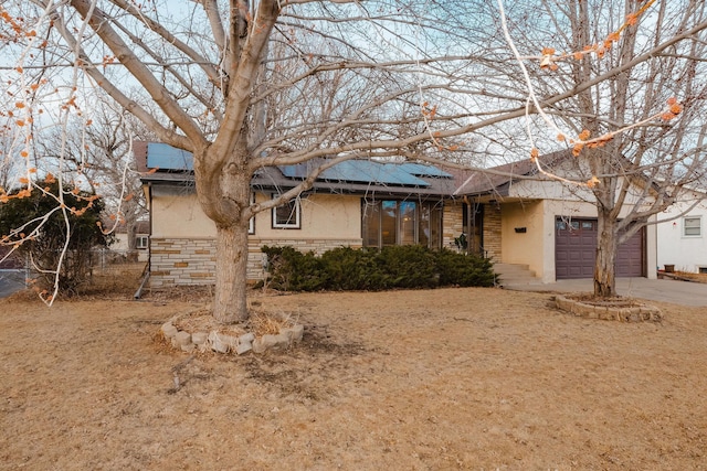 ranch-style house with an attached garage, stucco siding, concrete driveway, stone siding, and roof mounted solar panels