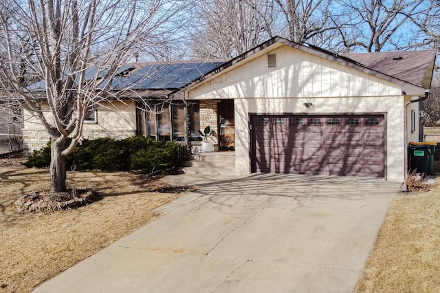 ranch-style house featuring solar panels, a garage, driveway, and a shingled roof