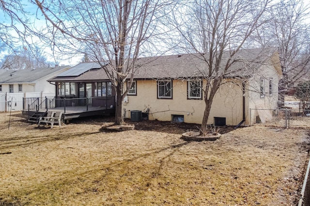 rear view of property featuring fence, a wooden deck, a shingled roof, stucco siding, and roof mounted solar panels