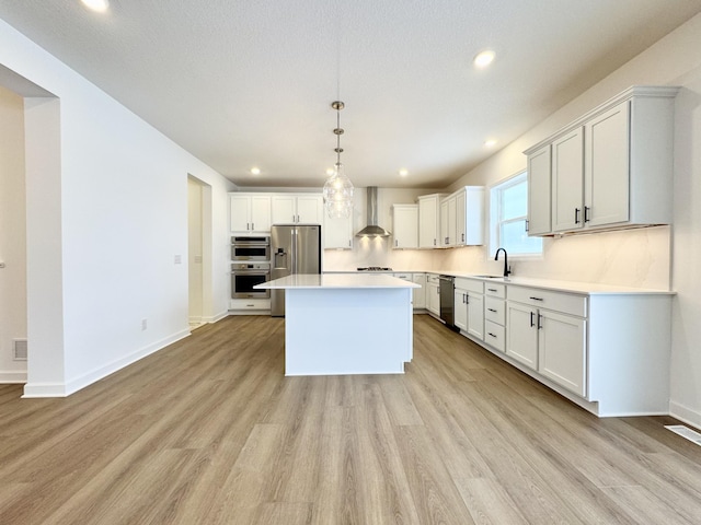 kitchen featuring light wood finished floors, stainless steel appliances, wall chimney exhaust hood, and light countertops