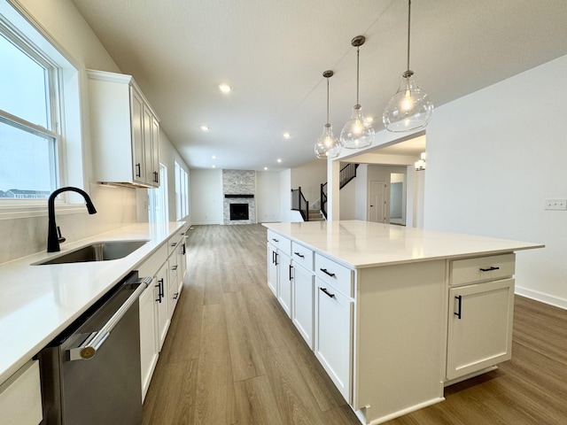 kitchen with a sink, wood finished floors, open floor plan, a large fireplace, and dishwasher