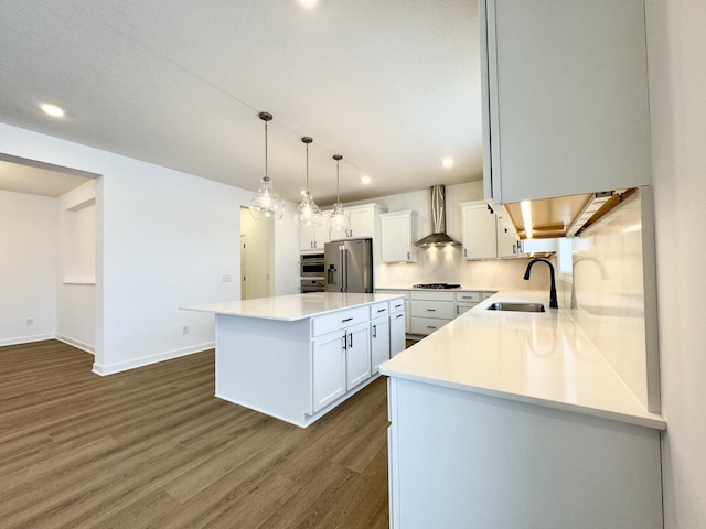 kitchen with a sink, gas cooktop, a kitchen island, stainless steel fridge, and wall chimney exhaust hood