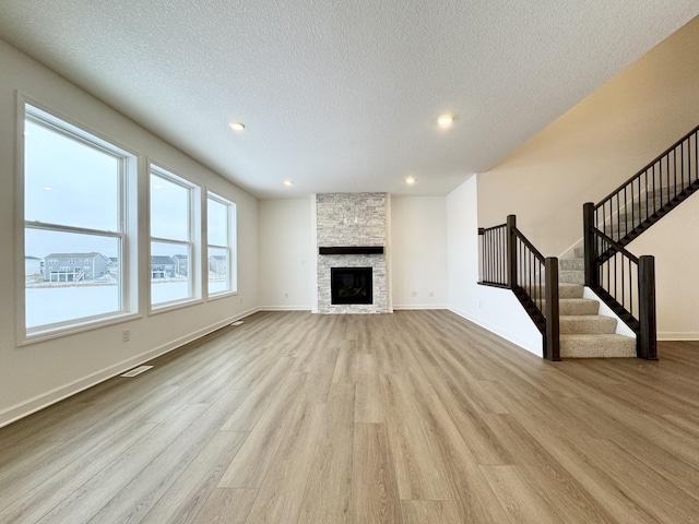 unfurnished living room featuring visible vents, wood finished floors, a stone fireplace, baseboards, and stairs