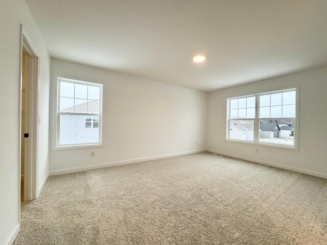 unfurnished room featuring light carpet, a textured ceiling, and baseboards