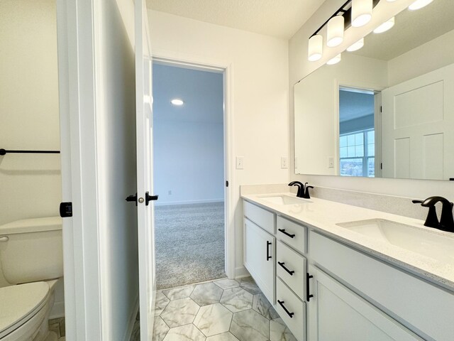 bathroom with double vanity, toilet, baseboards, and a sink