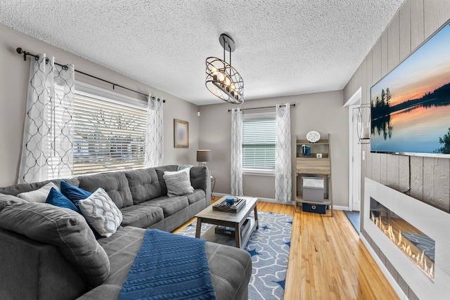 living area with baseboards, light wood-style floors, a glass covered fireplace, and a textured ceiling