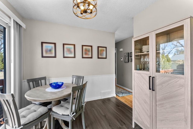 dining space with baseboards, visible vents, dark wood finished floors, a textured ceiling, and a notable chandelier