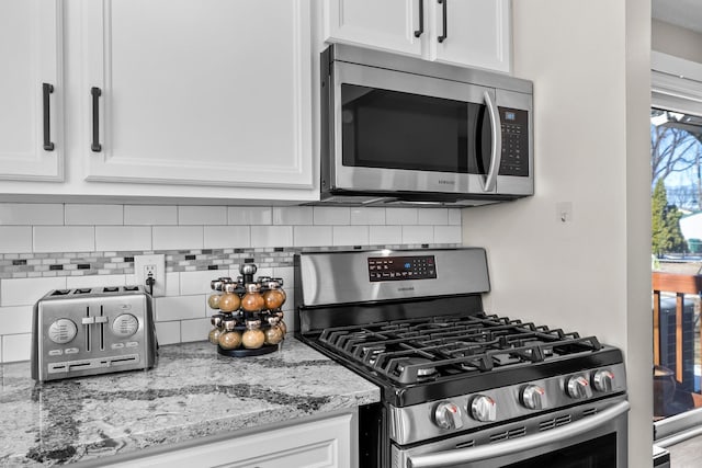 kitchen with decorative backsplash, white cabinets, light stone countertops, and appliances with stainless steel finishes