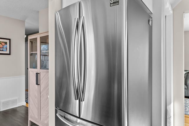 room details featuring a textured ceiling, wood finished floors, visible vents, freestanding refrigerator, and wainscoting