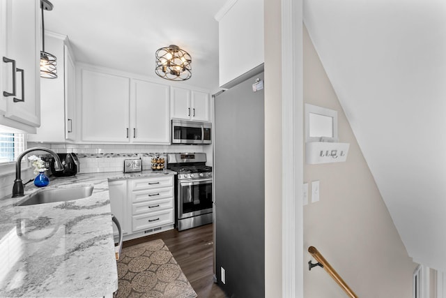 kitchen featuring dark wood finished floors, a sink, decorative backsplash, stainless steel appliances, and white cabinetry