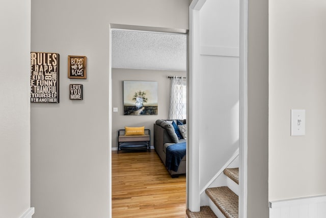 hall with light wood-style flooring, a textured ceiling, and baseboards