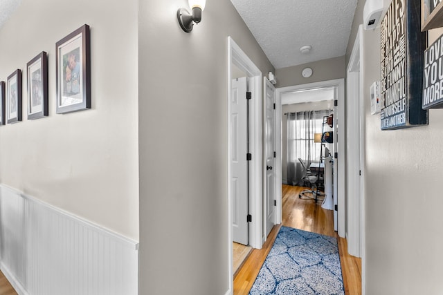 hall featuring a wainscoted wall, light wood-type flooring, and a textured ceiling