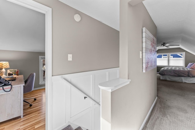 corridor featuring light wood finished floors, an upstairs landing, and vaulted ceiling