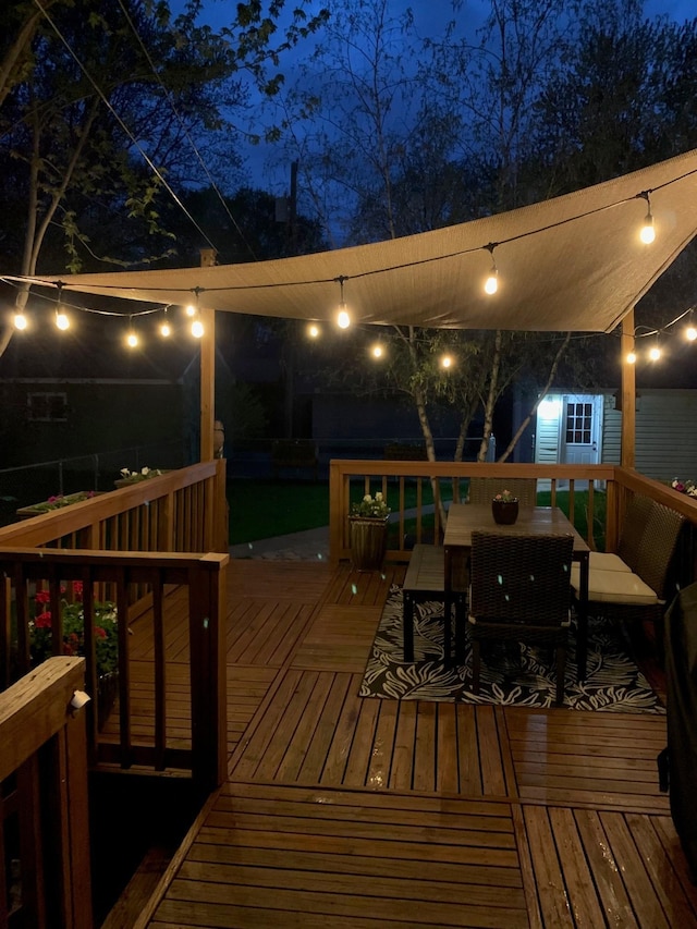 deck at night with outdoor dining area and an outdoor structure