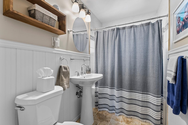 full bathroom featuring wainscoting, curtained shower, toilet, and stone finish flooring