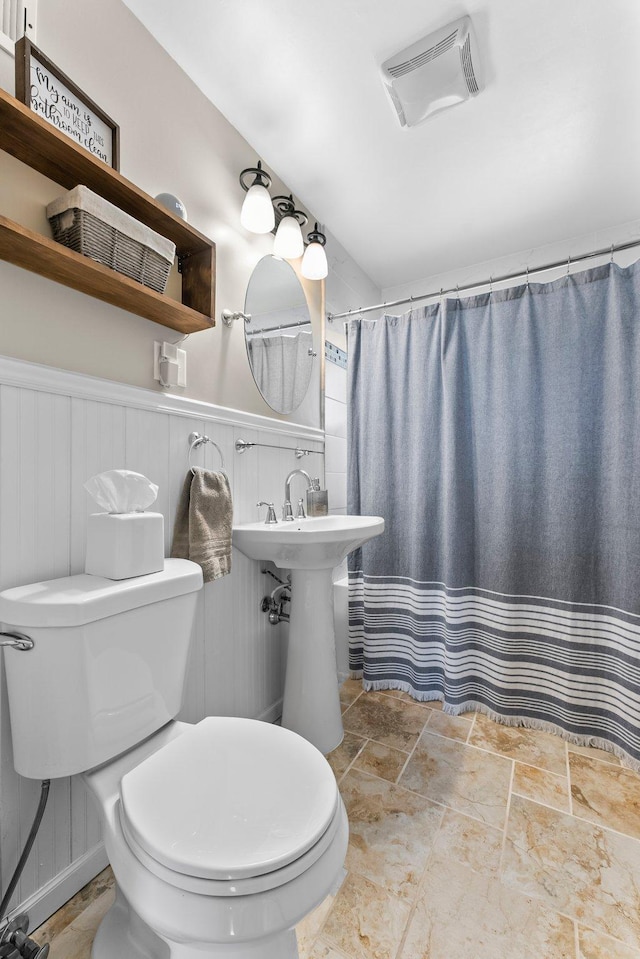 full bath with visible vents, curtained shower, stone finish flooring, a wainscoted wall, and toilet