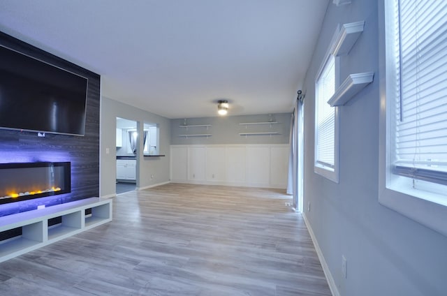 unfurnished living room with baseboards, a large fireplace, and light wood-style floors