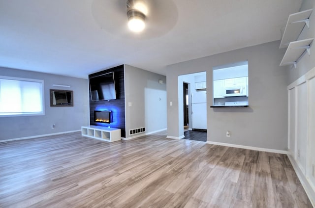 unfurnished living room featuring light wood finished floors, visible vents, a large fireplace, baseboards, and ceiling fan