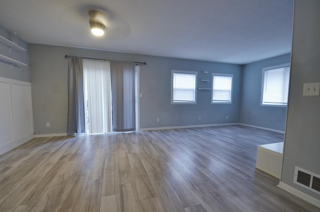 unfurnished living room with wood finished floors, visible vents, and baseboards