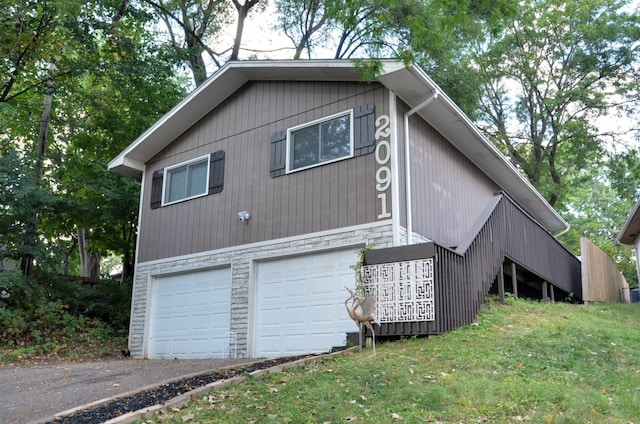 view of side of home with driveway, a yard, a garage, and stone siding