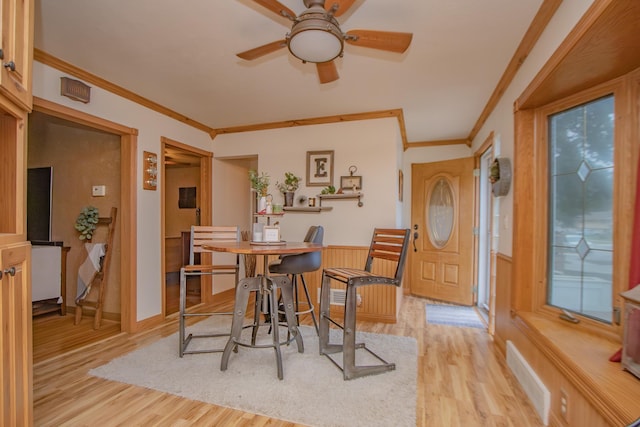 dining room with ceiling fan, light wood-style flooring, wainscoting, and ornamental molding