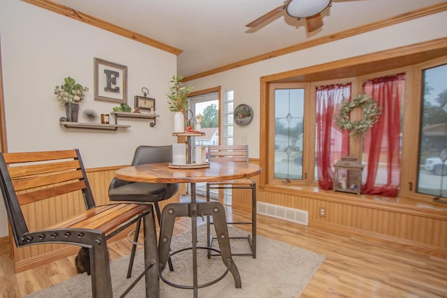 dining space featuring light wood-type flooring, visible vents, wainscoting, crown molding, and ceiling fan