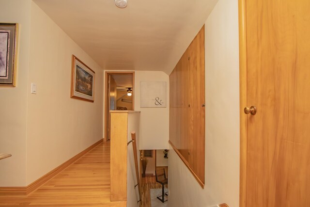 hallway featuring baseboards, an upstairs landing, and light wood-style flooring