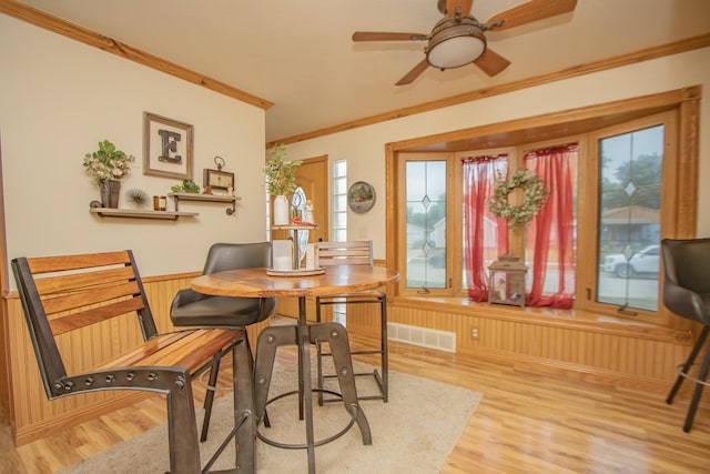 dining space with wooden walls, visible vents, a wainscoted wall, ornamental molding, and light wood-style floors