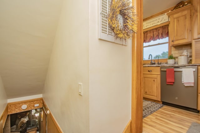 interior space featuring a sink, light wood-type flooring, stainless steel dishwasher, and decorative backsplash