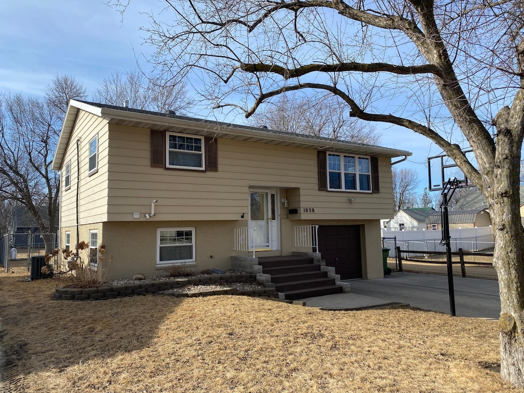split foyer home featuring central air condition unit, a garage, concrete driveway, and fence
