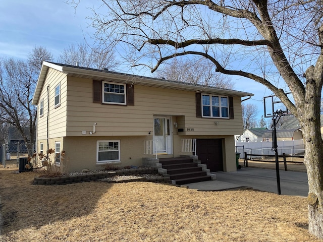 split foyer home featuring central air condition unit, a garage, concrete driveway, and fence