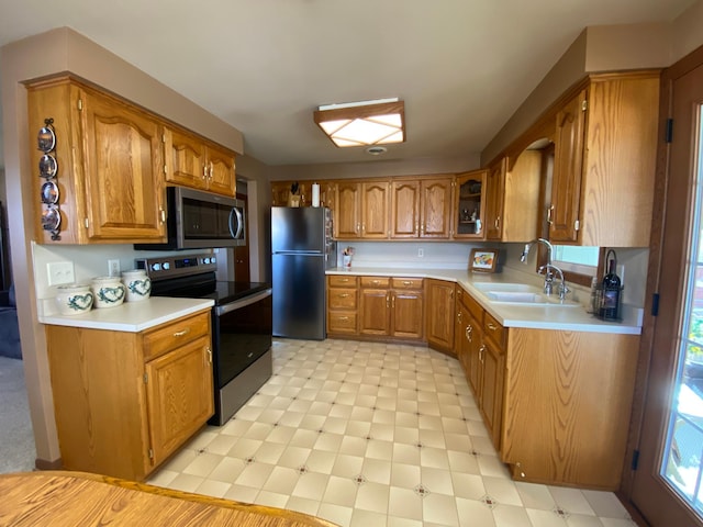 kitchen featuring light floors, a sink, stainless steel appliances, light countertops, and brown cabinets