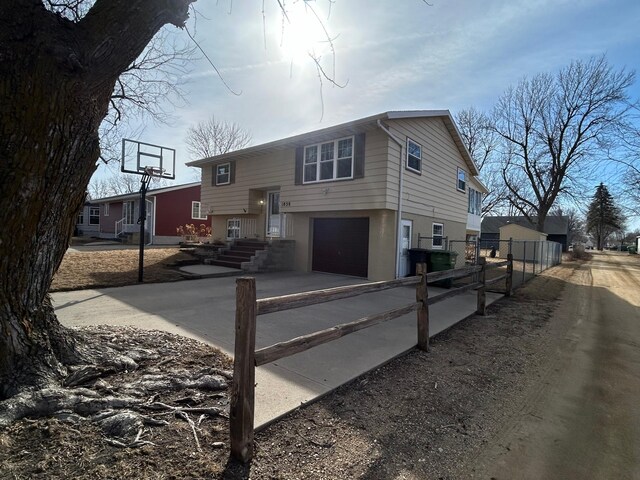 split foyer home with an attached garage, fence, driveway, and stucco siding