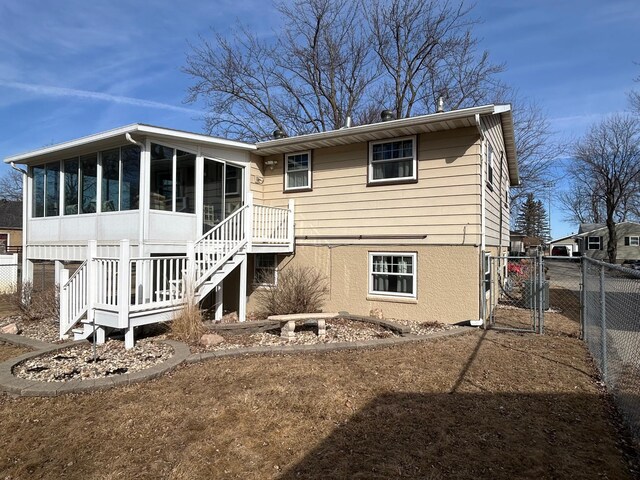 back of property featuring fence, stairway, stucco siding, a sunroom, and a gate