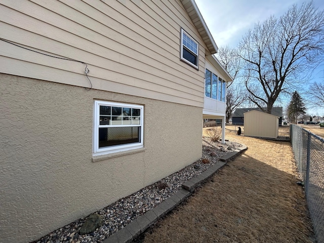 view of side of property with a storage unit, fence, an outbuilding, and stucco siding