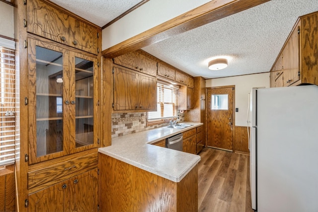 kitchen featuring light countertops, brown cabinets, freestanding refrigerator, wood finished floors, and stainless steel dishwasher